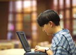 Boy works alone at laptop in library